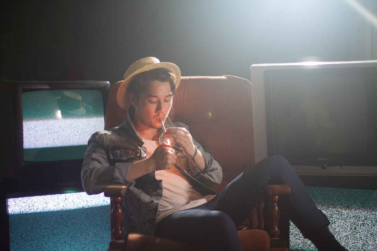 Tom lighting a cigarette on a couch with TVs